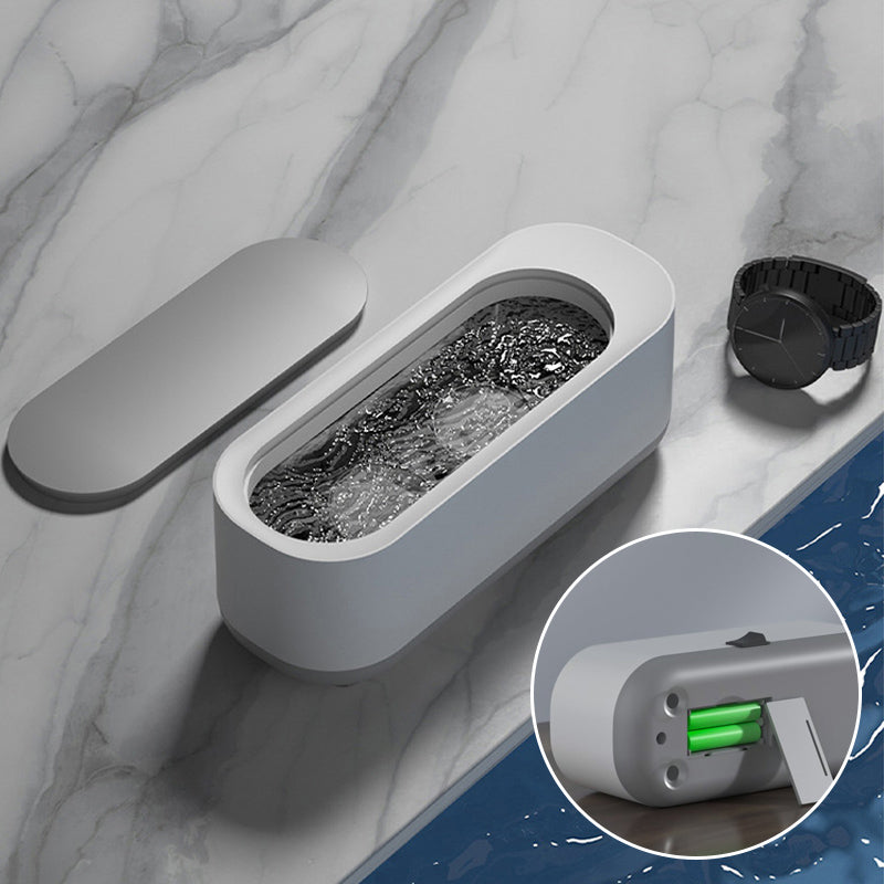Kompakt hvid-grå ultralyd renser til dybderensning; fjerner snavs fra briller og smykker med højfrekvent vibration