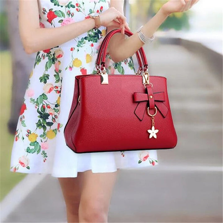 Dame skuldertaske med blomsterhåndtag, struktureret tote-stil, skinnende finish, justerbar rem.