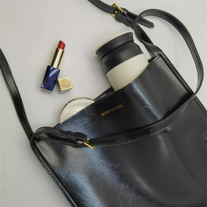 Stilfuld dame skuldertaske i skinnende kunstlæder, rummelig indvendig, justerbar rem, luksuriøst look.
