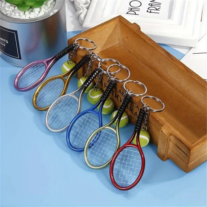 Farverig mini tennisracket nøglering i seks farver: rød, grøn, lilla, sølv, guld og blå.